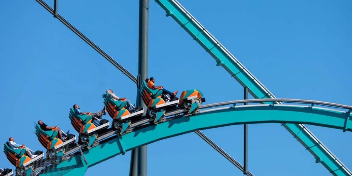 Roller coaster train ascending the teal track at the amusement park.