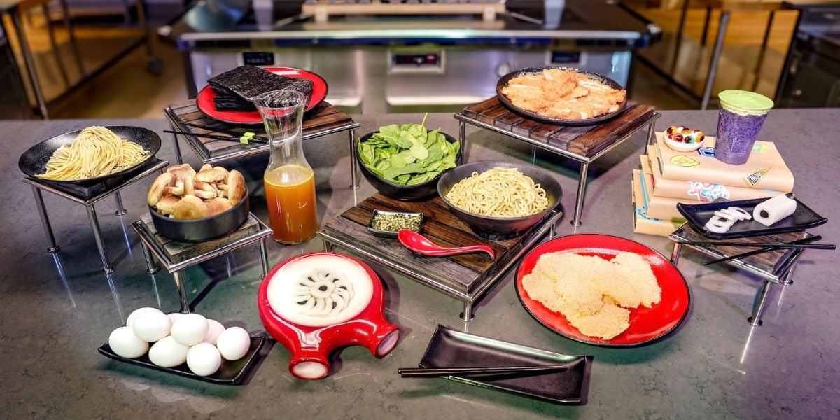A spread of ramen ingredients for a Monstropolis-inspired meal at Monsters, Inc. Laugh Floor, including noodles, broth, pork, eggs, and spinach.