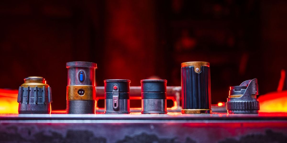 Six custom lightsaber hilt components from Savi’s Workshop at Star Wars: Galaxy’s Edge lined up on a table.