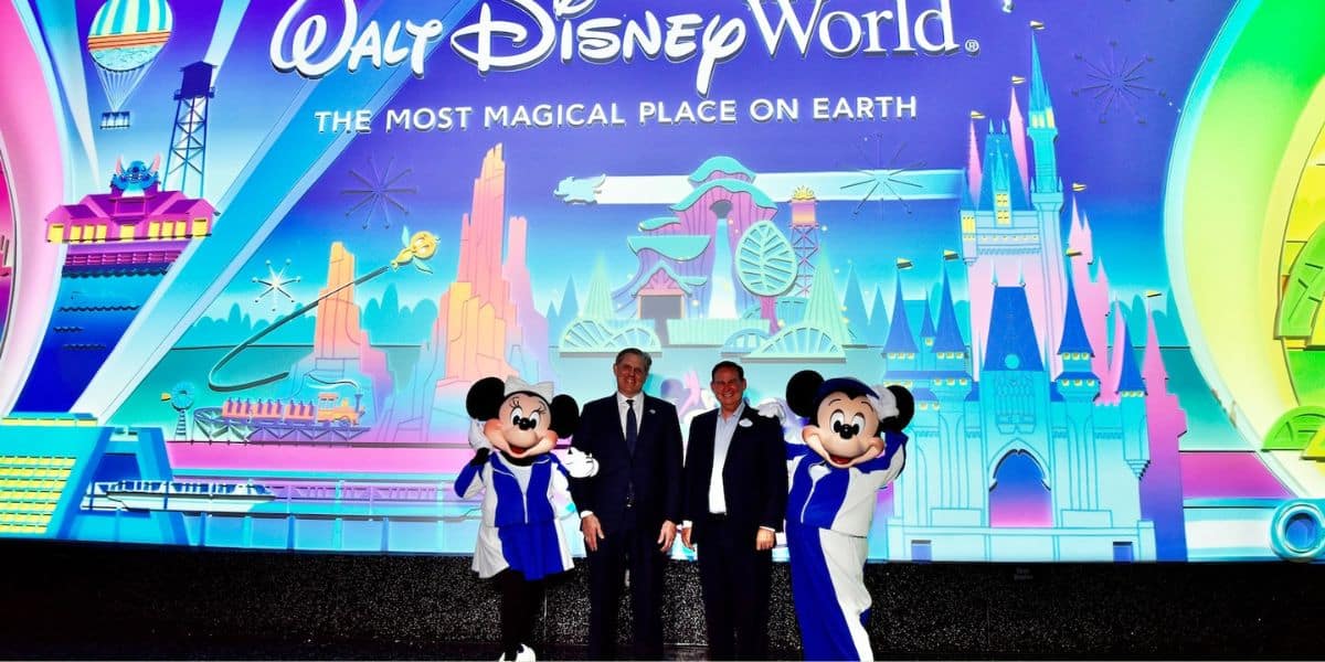 Mickey and Minnie Mouse pose with two men in suits in front of a Walt Disney World sign.